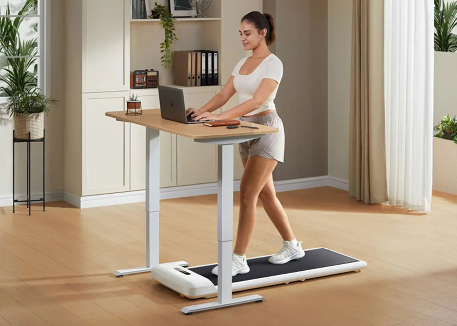 Woman using a WalkingPad C2 under-desk treadmill while working on a laptop at a standing desk